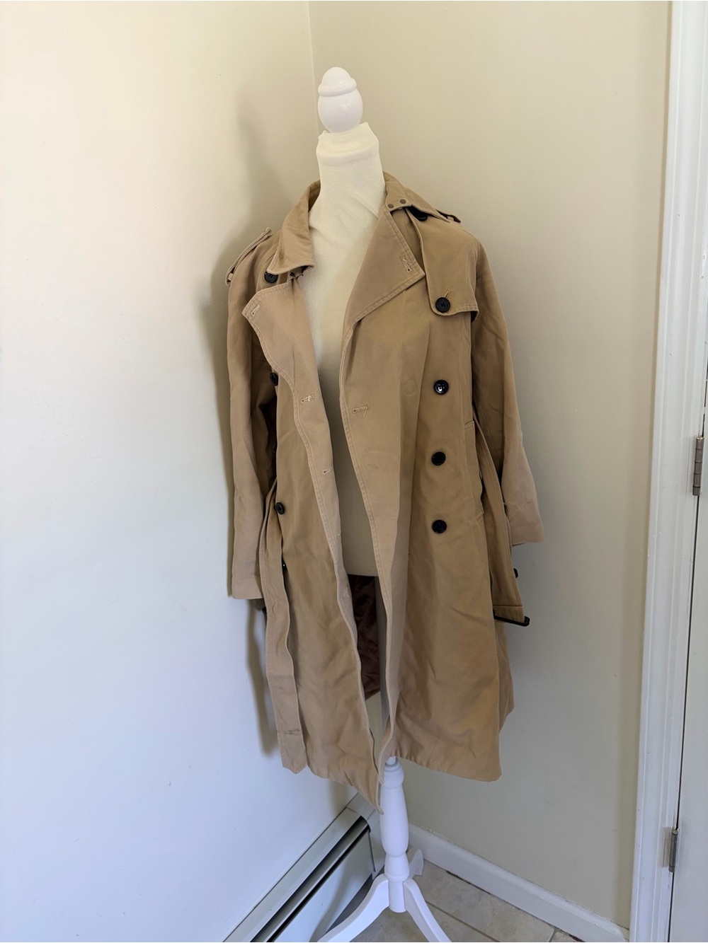 Beige trench coat features a double-breasted button closure and classic lapels